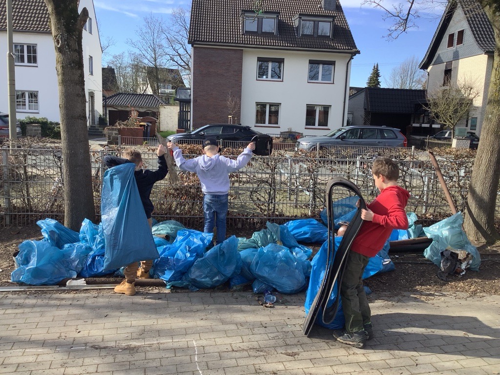 Drei Kinder halten unvorstellbar große Müll-Fundstücke hoch: Autoteile, Eisenrohre